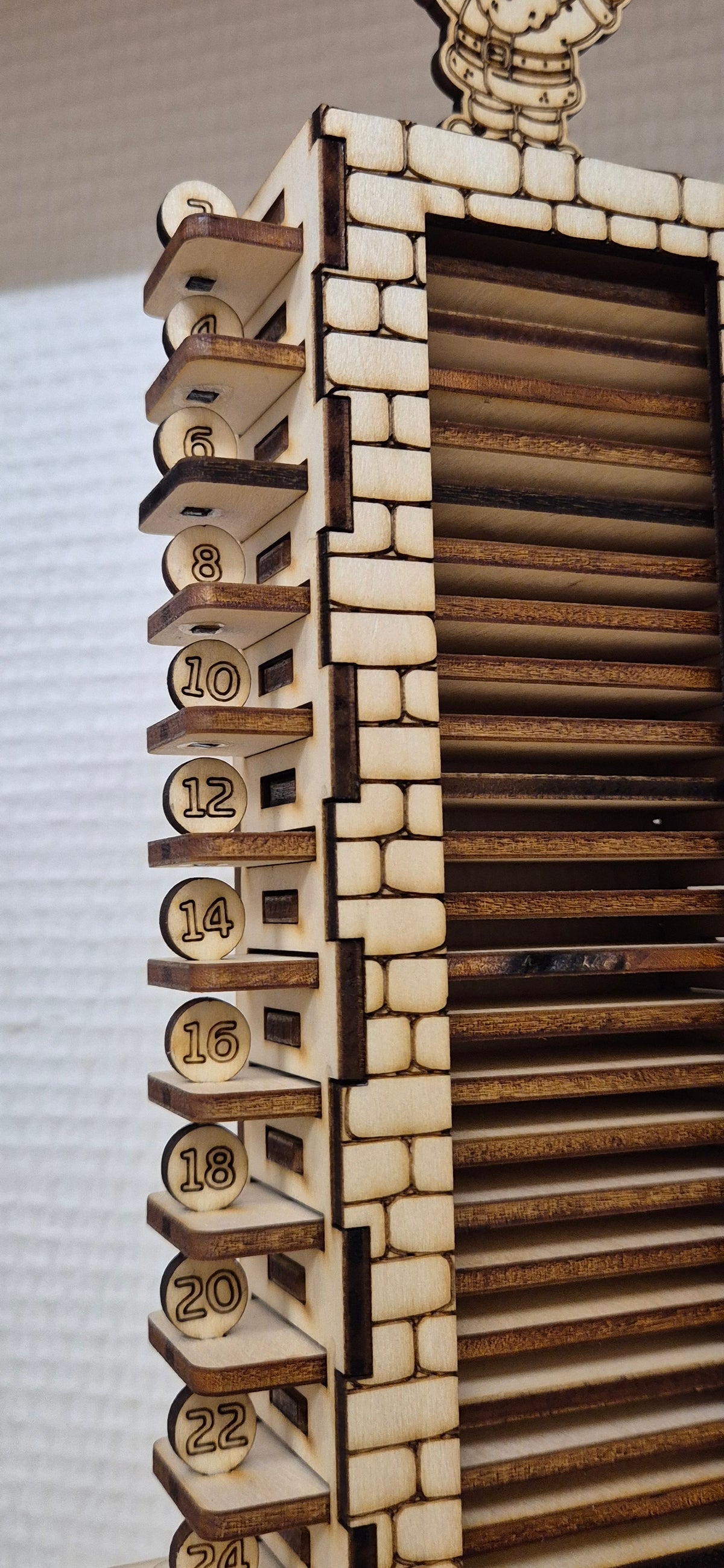 Detalje af julekalenderens nummererede stave og murstensmønster i træ.