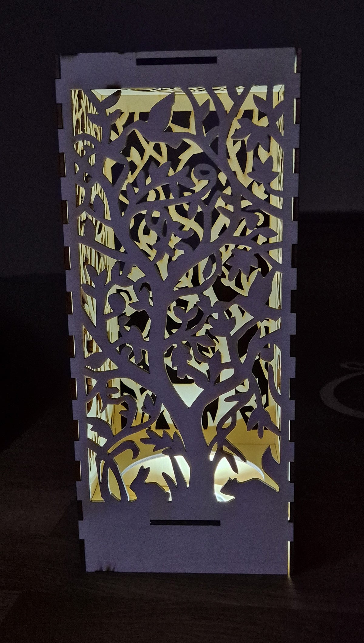 Lanterne med lys gennem laserskårne grene og blade.